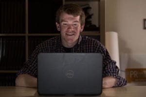 Smiling man using laptop in dimly lit room.