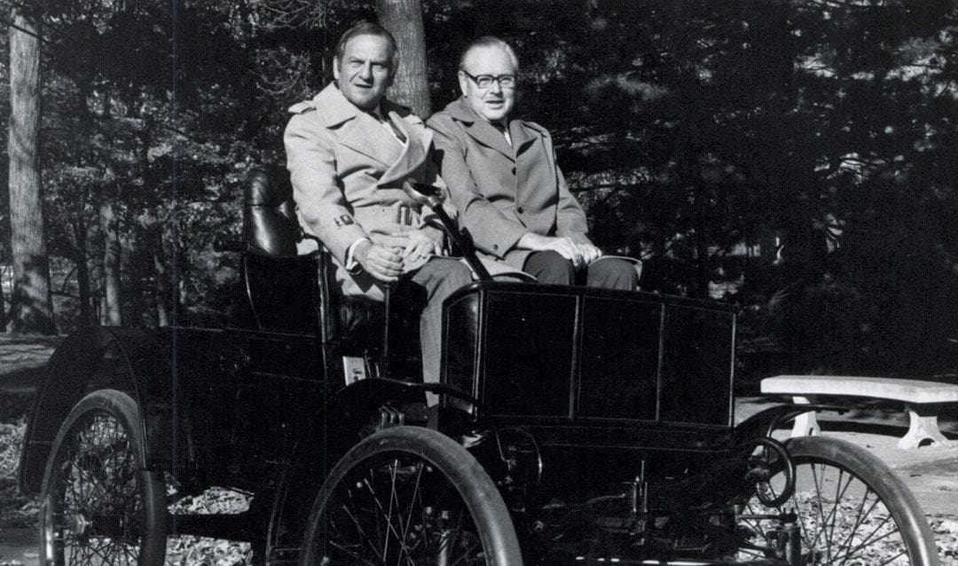Lee Iacocca Two men seated in vintage automobile outdoors.
