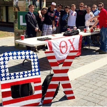 Fraternity event with students at outdoor table.