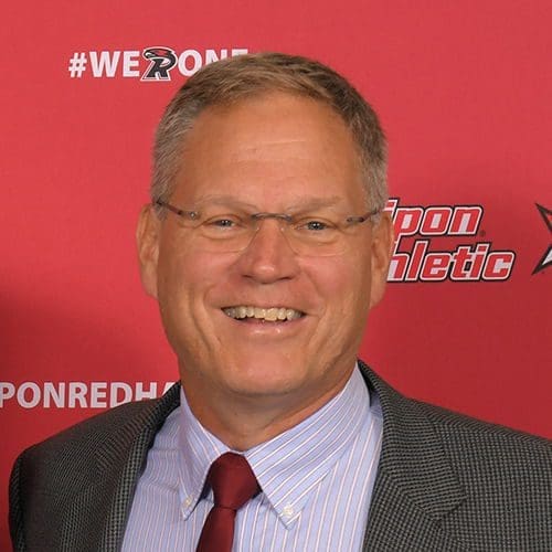 Smiling man in suit at promotional event backdrop.