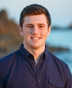 Young man smiling by the ocean at sunset.