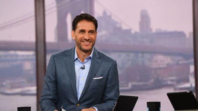 Mike Greenberg Smiling man in a suit on a broadcast set.