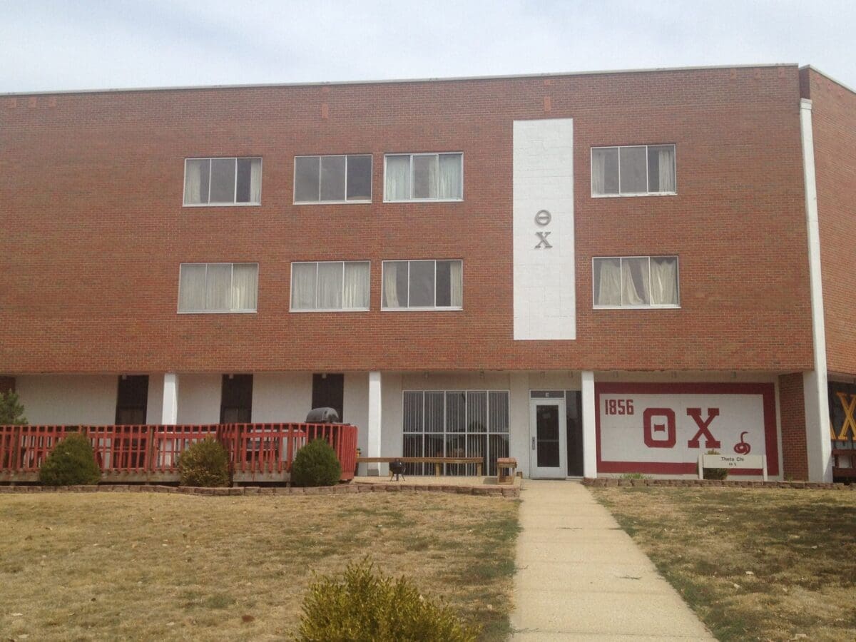 Brick building with Greek letters and outdoor seating.