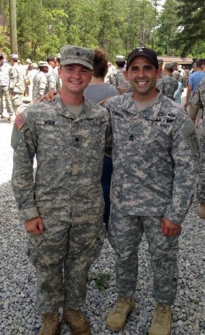 Two soldiers in military uniforms smiling together.