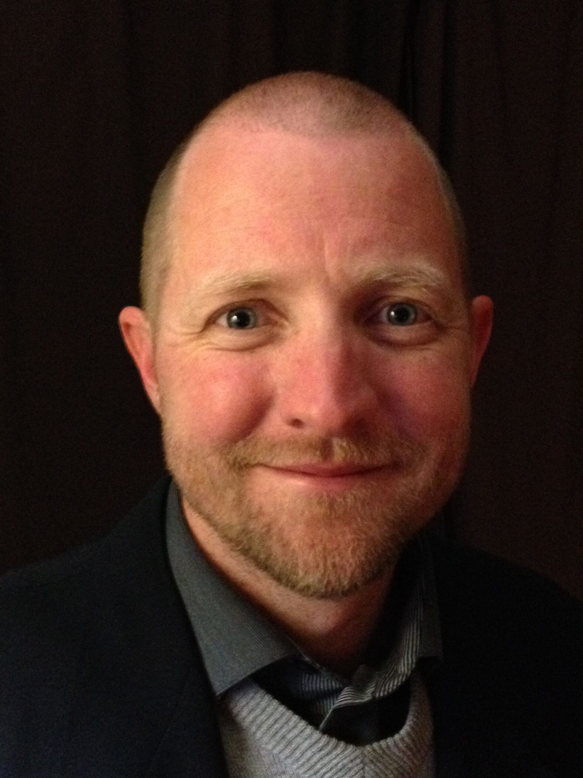 Smiling man in a suit against a dark background.