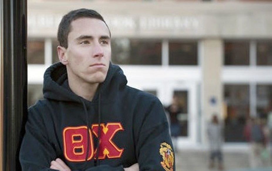 Young man in hoodie outside university building.