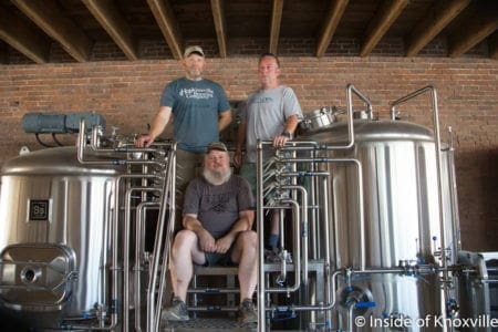 Brewers posing with brewing equipment in a brewery.