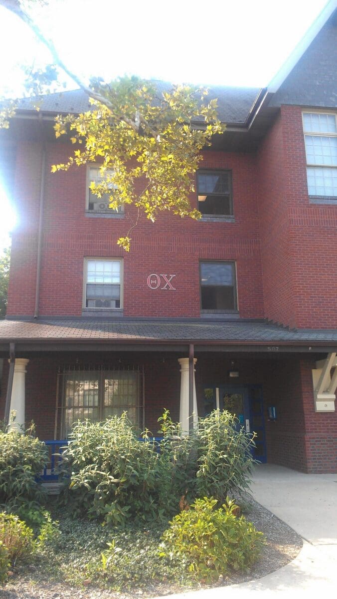 Brick building with windows and greenery in front.