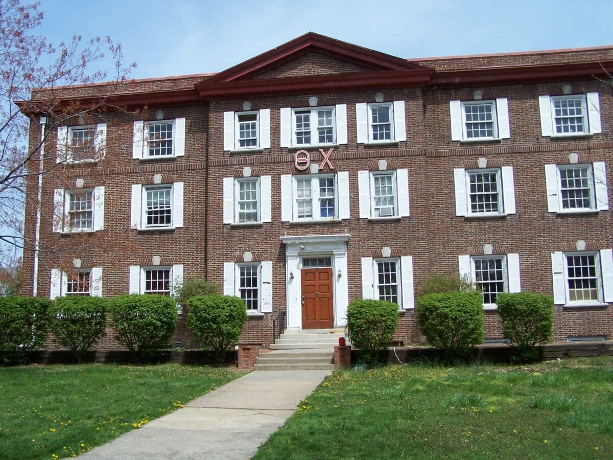 Historic brick fraternity house with white shutters.