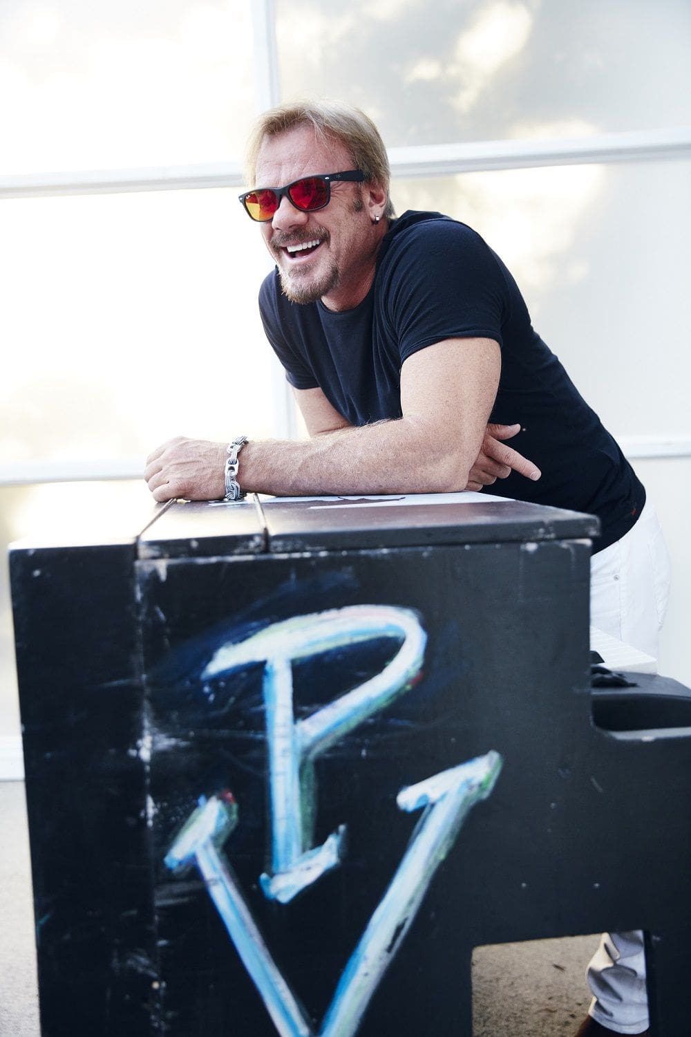 Phil Vassar Man in sunglasses smiling next to a piano.