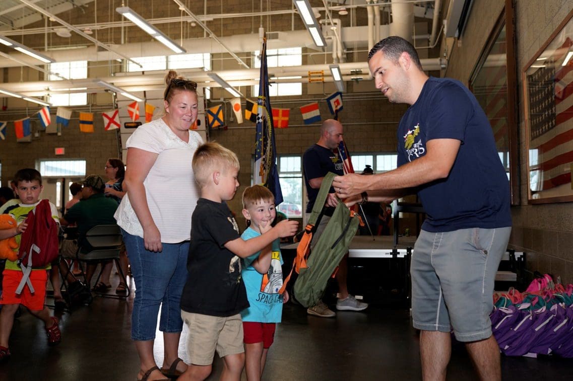 Children receiving backpacks at community event.