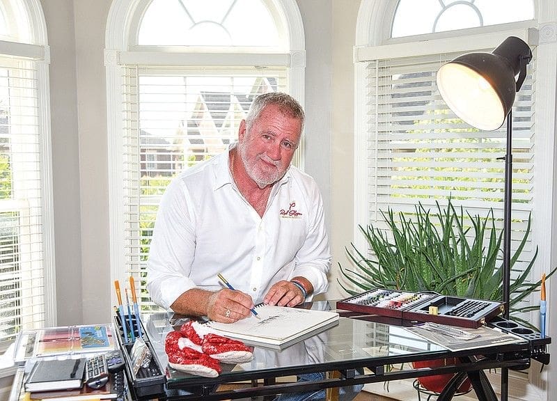 Man sketching at a desk with art supplies.