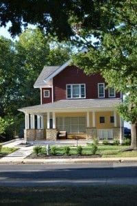 Two-story red house with porch and landscaping.