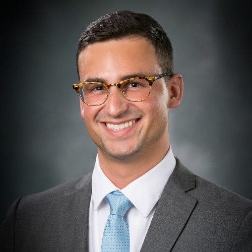 Gamma Tau - Drake - Raymond Starks Smiling professional man in suit and glasses.