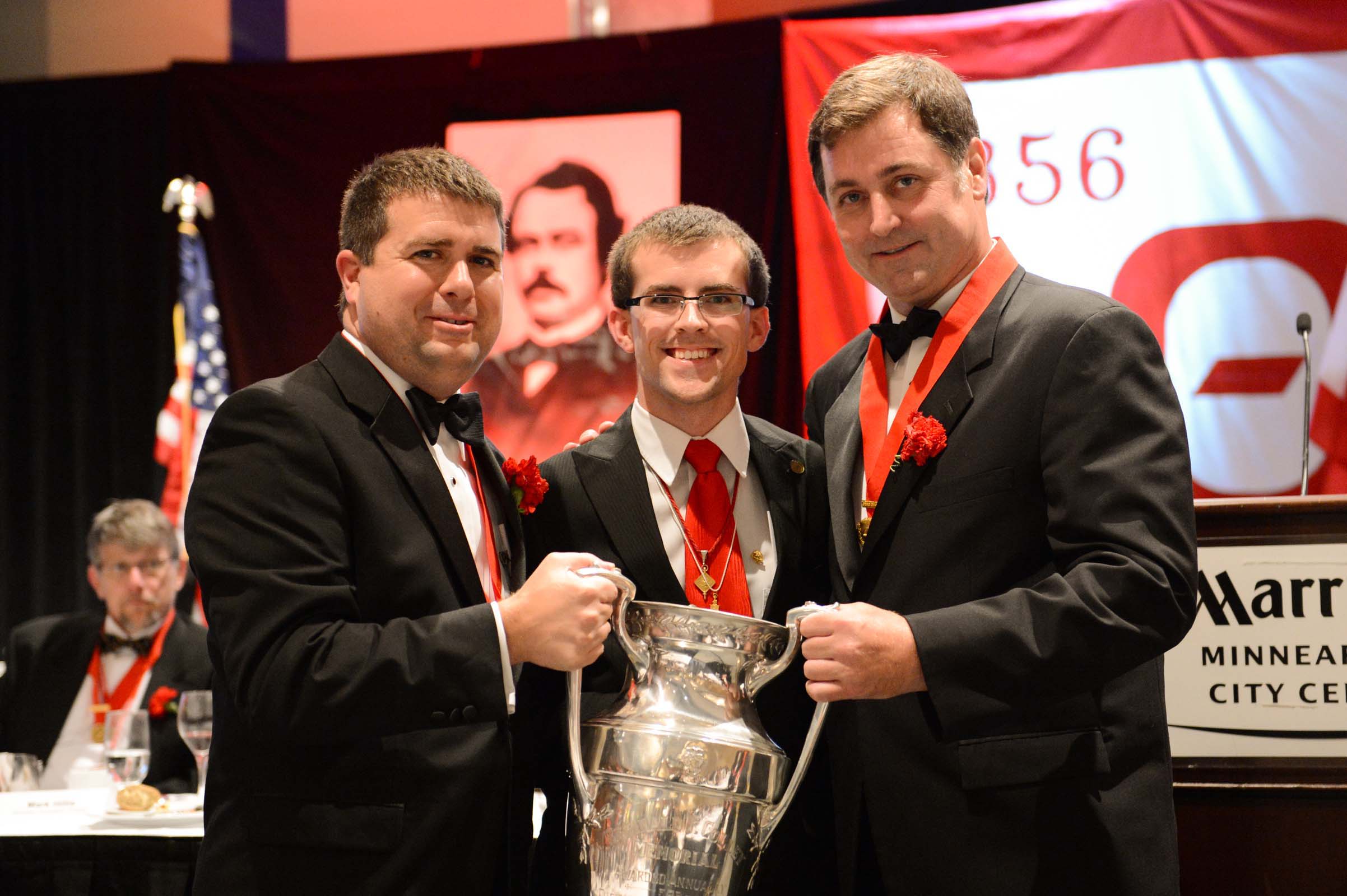 Men in tuxedos holding a trophy at an event.