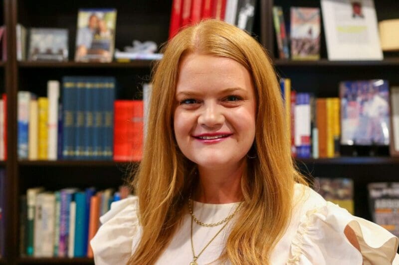 Smiling woman with long hair in library setting.