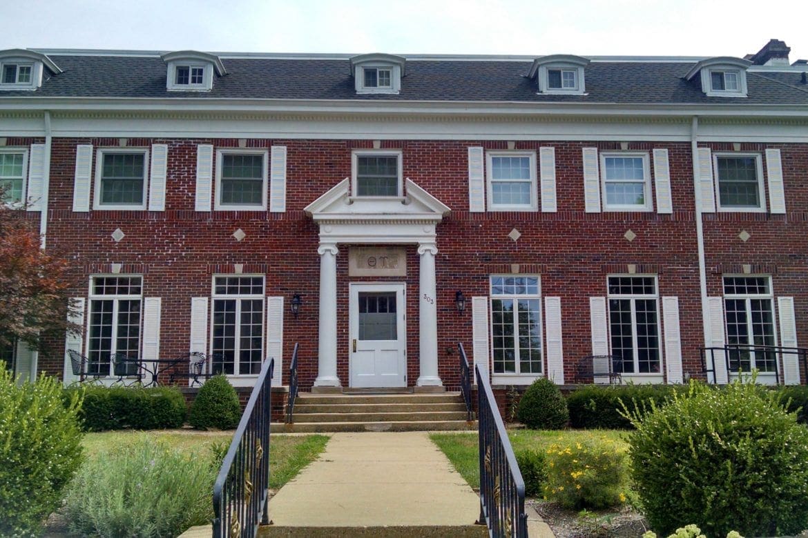 Brick building with grand entrance and landscaped yard.