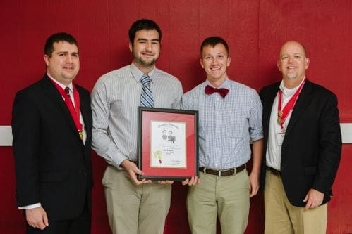Four individuals holding an award certificate together.