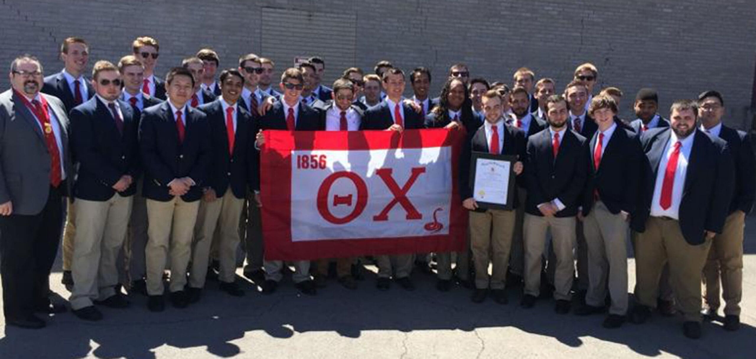 Group of fraternity members holding flag and certificate.