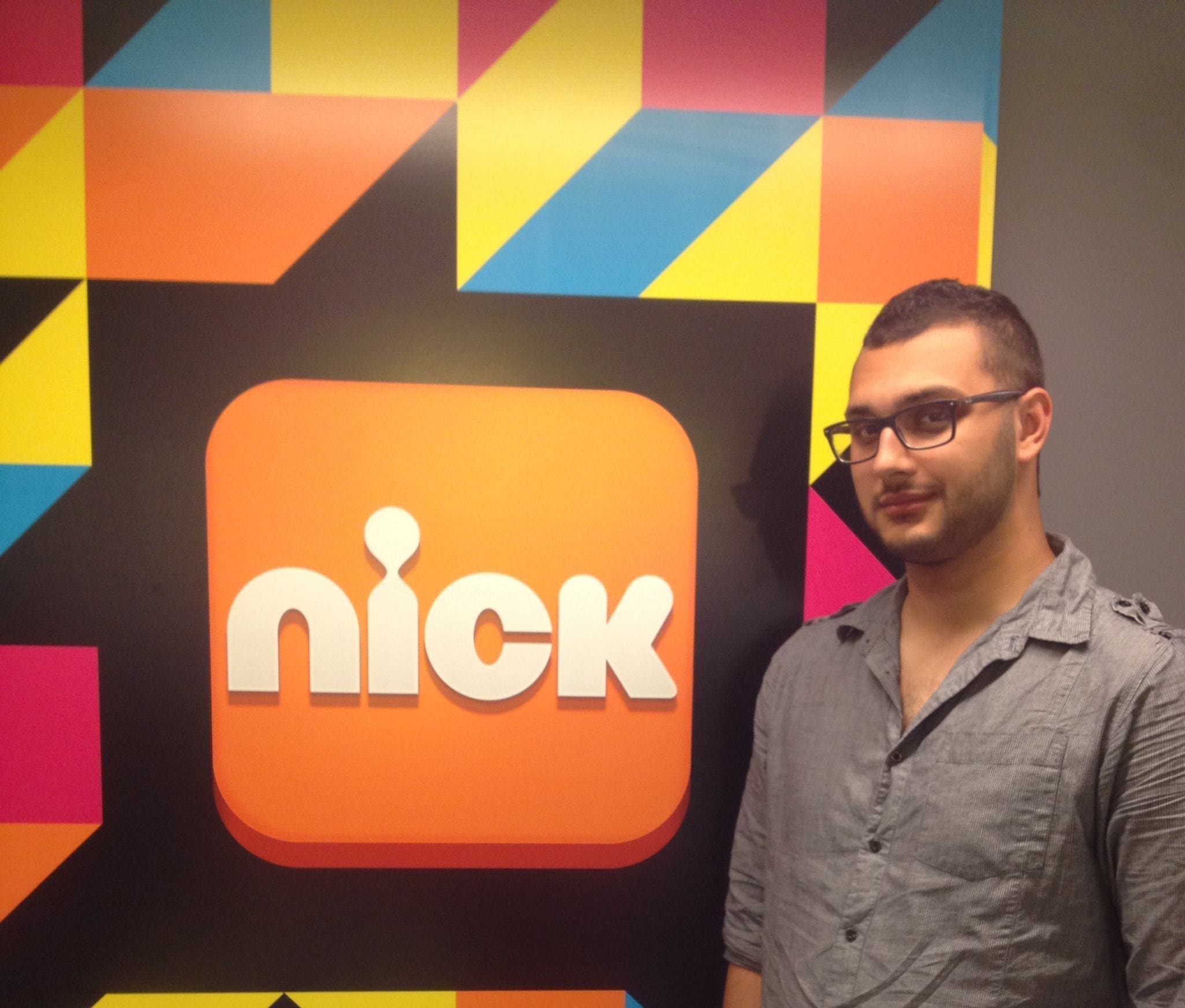 Person standing beside Nick logo on colorful wall.