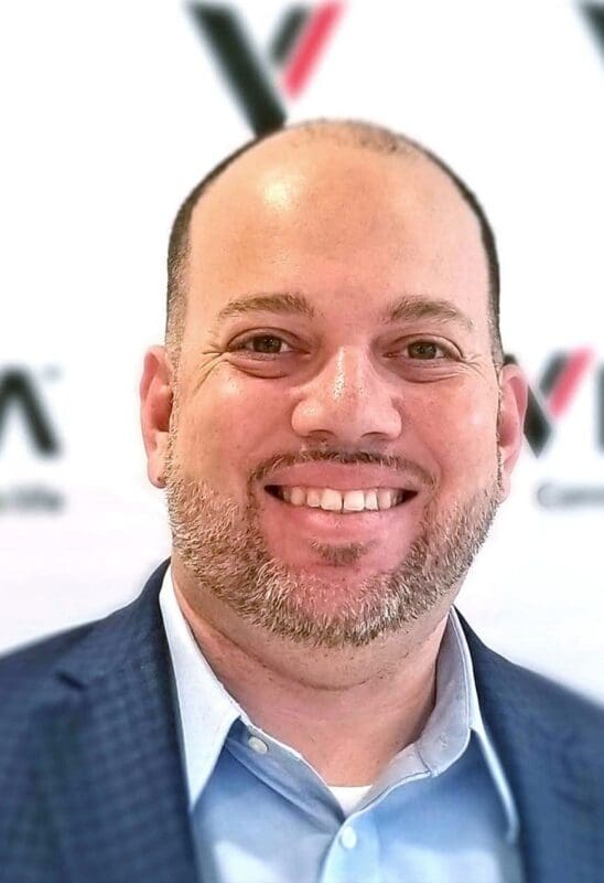 Smiling man in a blue suit against a logo backdrop.