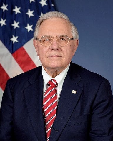 Official portrait of a government official with American flag.