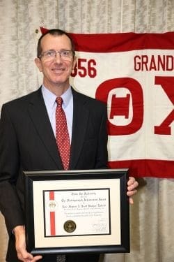 Man holding award certificate with banner in background.