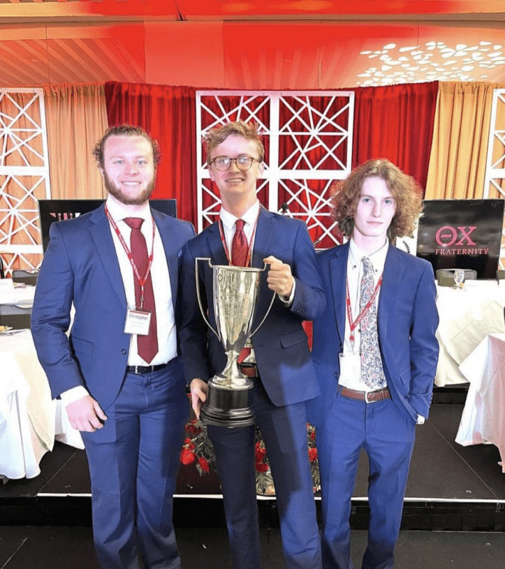 Three young men in suits holding a trophy.
