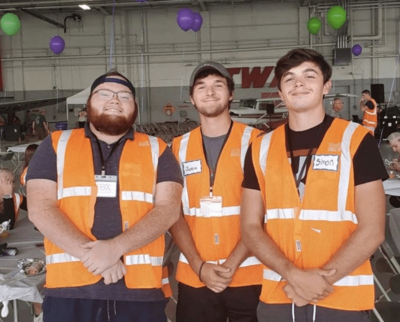 Three workers in safety vests smiling indoors.