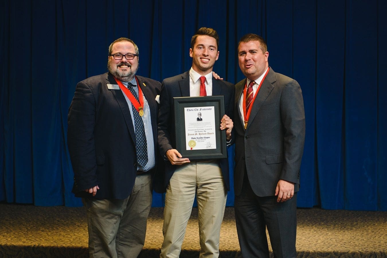Three men holding award certificate on stage.