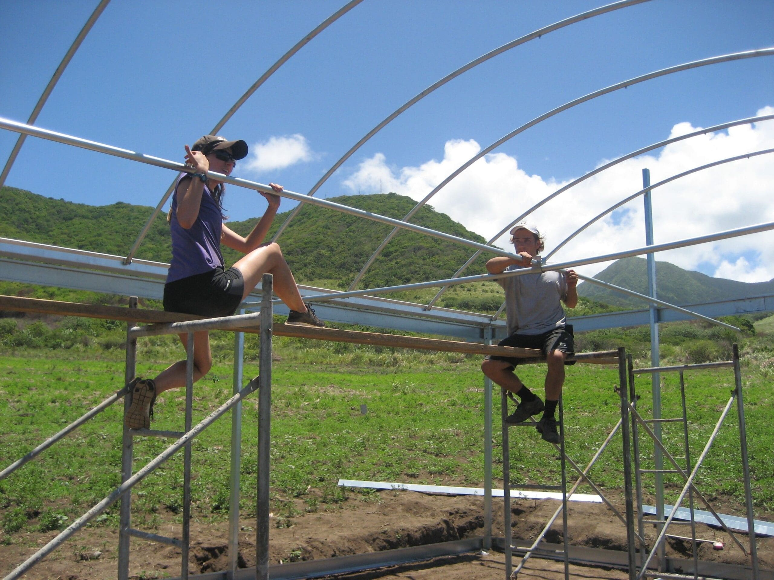 Two people constructing a greenhouse frame outdoors.