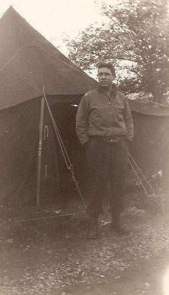 Man standing outside military-style tent.