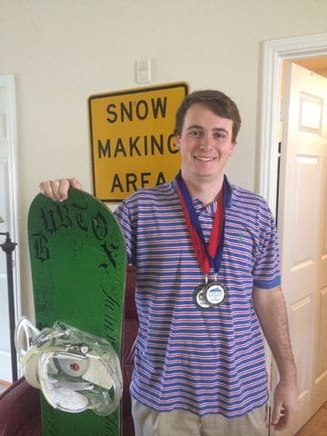 Smiling young man with snowboard and medals.