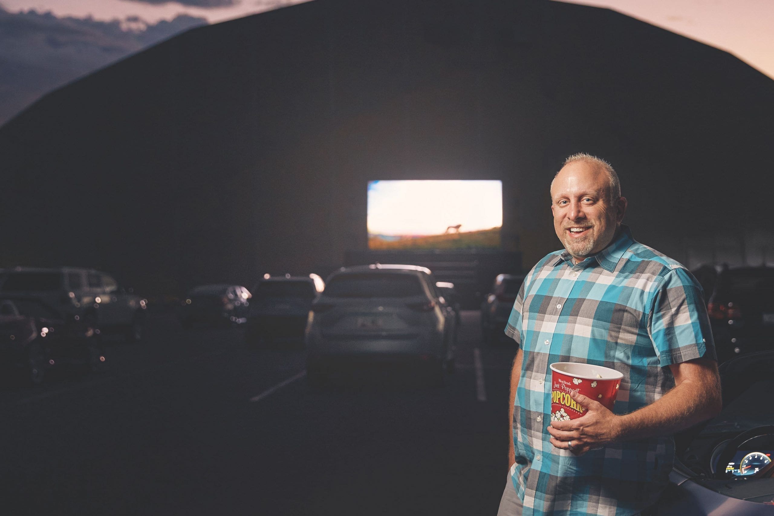 Steve LeVine Man enjoying outdoor movie with popcorn at drive-in.
