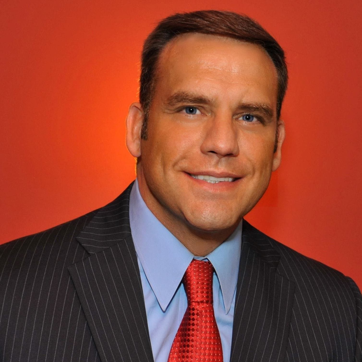 Man in suit with red tie against orange background.