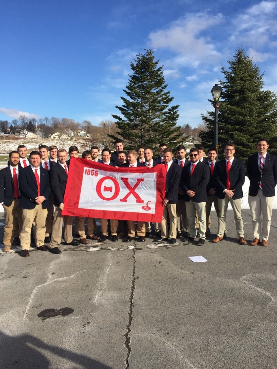 Group of men in blazers holding a fraternity flag.
