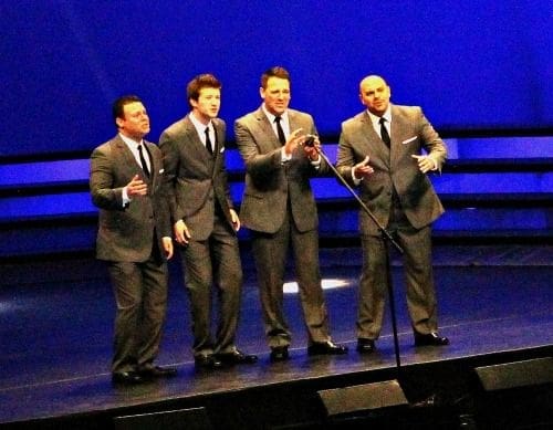 Four men performing in suits on stage.