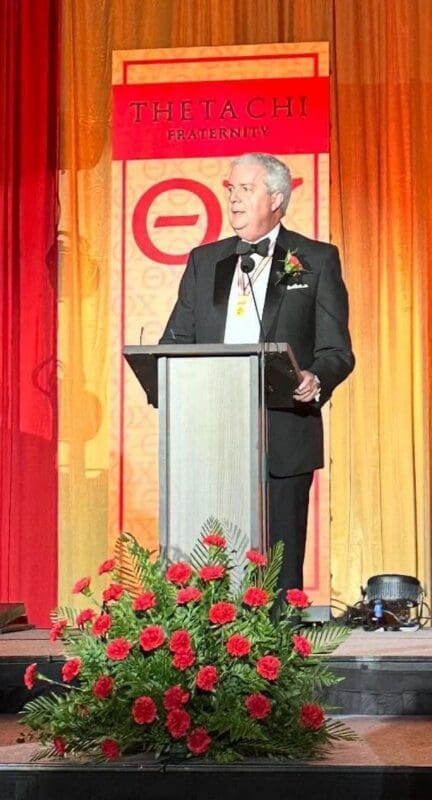 Man speaking at Thetachi Fraternity event podium.