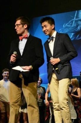 Two presenters on stage with microphones at event.
