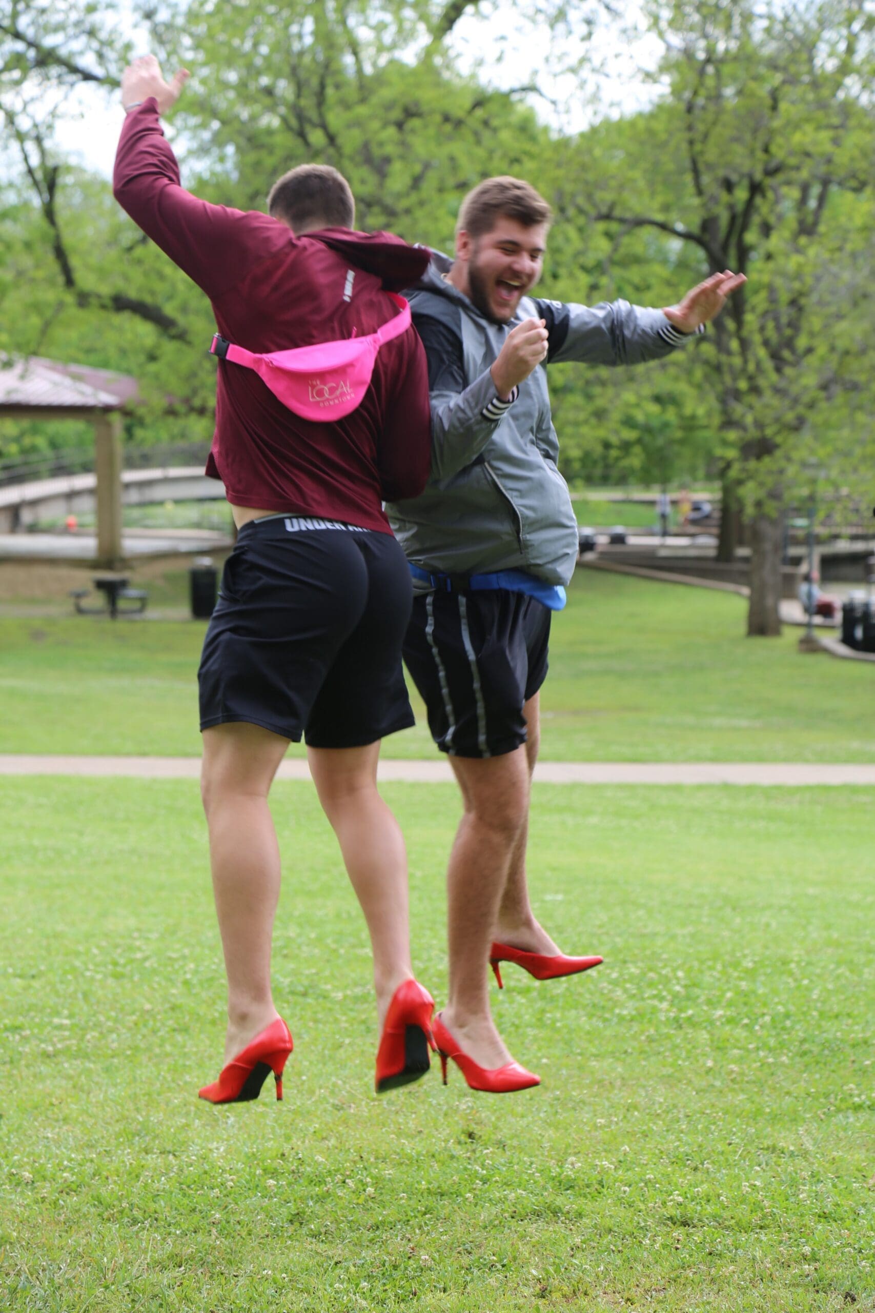Iota Upsilon/Texas State Two people wearing high heels jumping in a park.