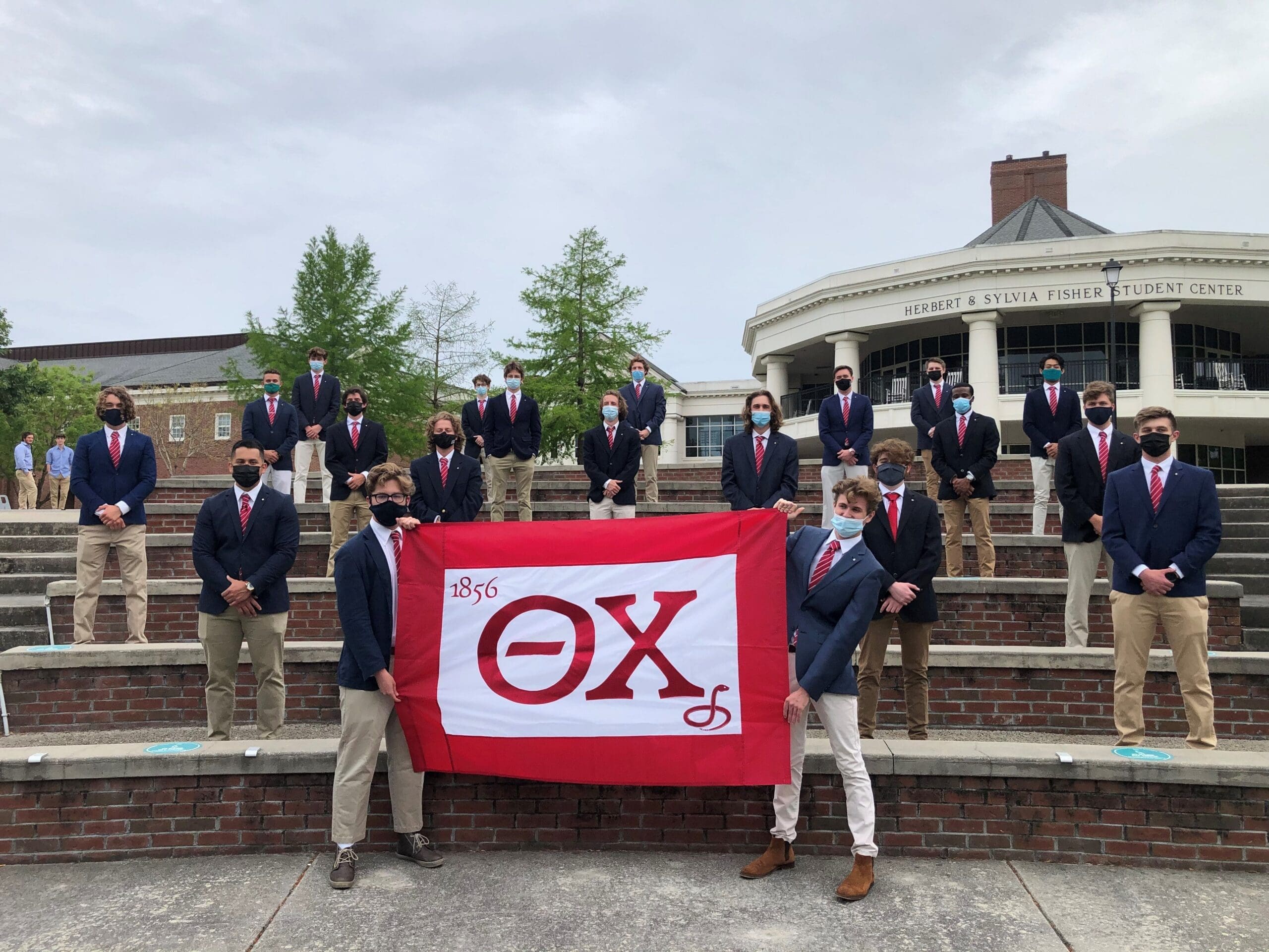 Iota Alpha Recolonized Group of students posing with fraternity flag outdoors.