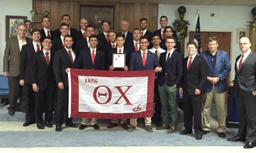 Group of fraternity members holding flag and certificate.