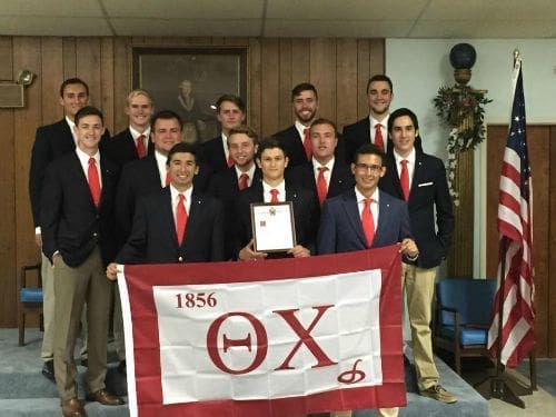 Group photo of fraternity members holding Theta Chi flag.