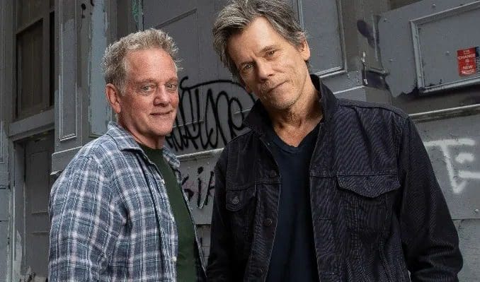 Two men posing in front of graffiti wall.
