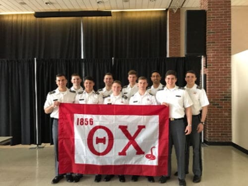 Group of cadets holding a fraternity flag.