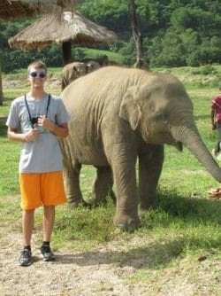 Young man standing beside an elephant in nature.