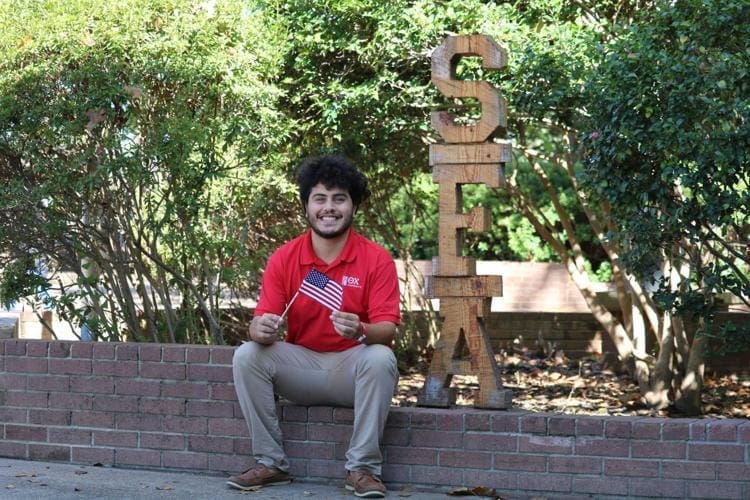 Victor Torres - SFA Student holding American flag next to SFA sign.
