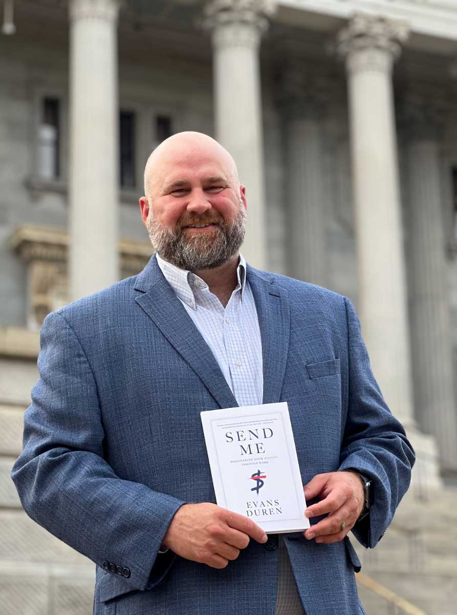Author holding "Send Me" book outside government building.