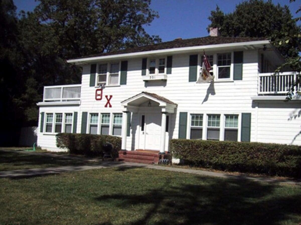Historic white fraternity house with green shutters.