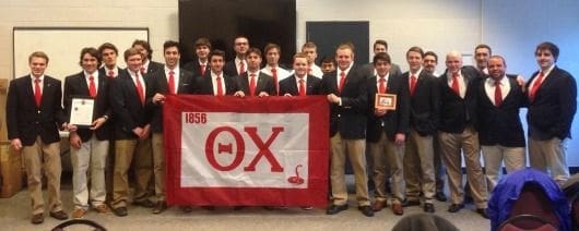 Fraternity members posing with flag and award.